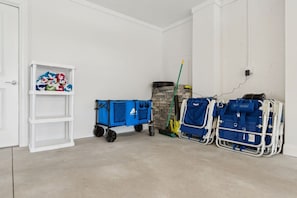 Ein Zimmer mit einer weißen Tür, einem weißen Regal voller bunter Gegenstände, einem blauen Wagen, einem Besen und einer Steckdose.