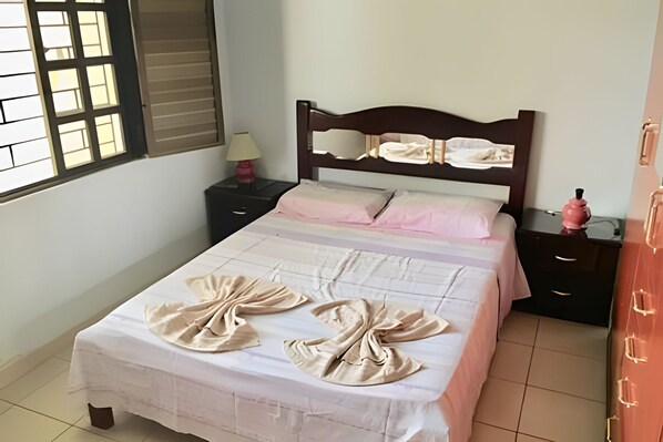 Un lit bien fait, recouvert d’une couvre-lit blanche et agrémenté de deux coussins décoratifs de couleur beige.