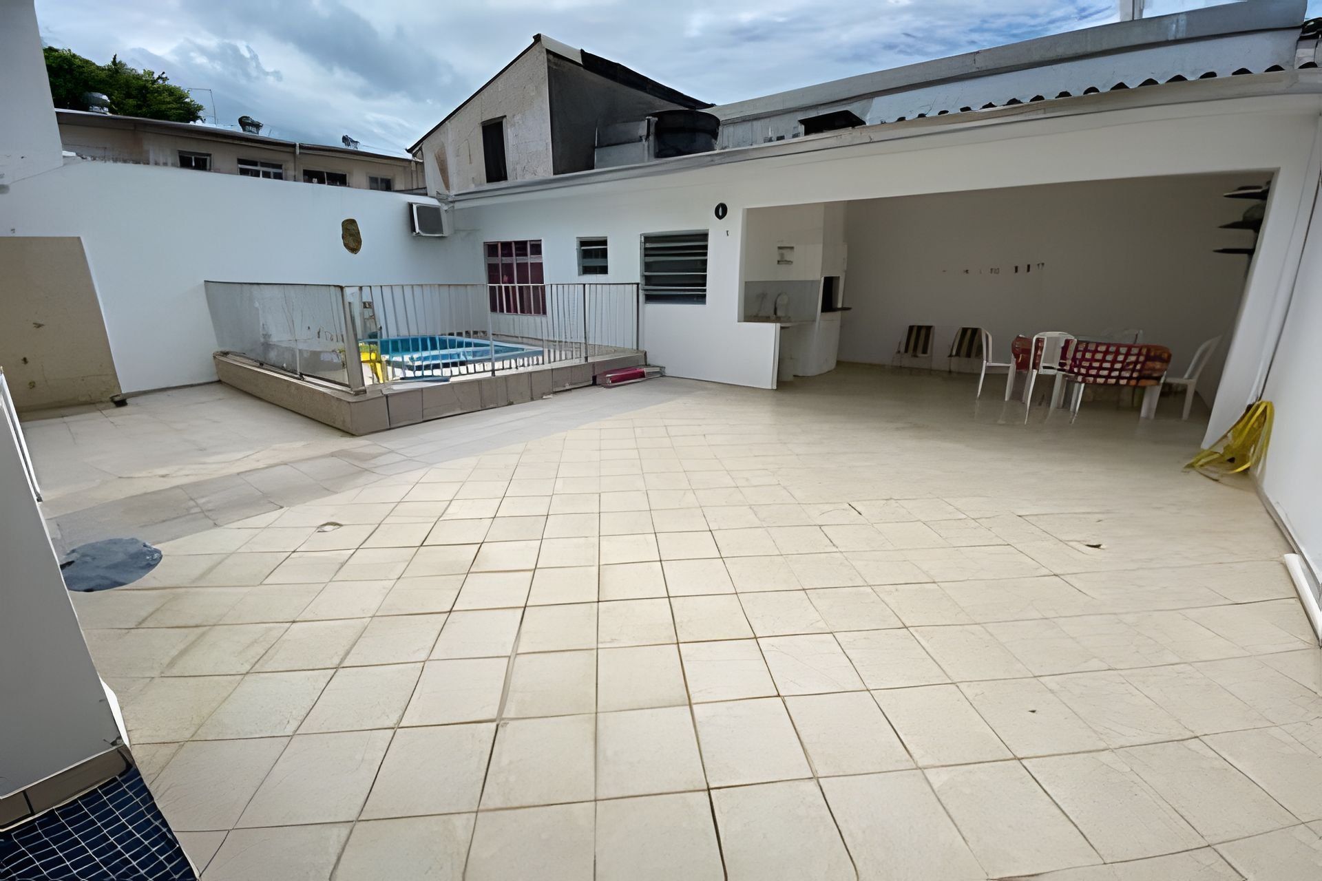 Ampla área externa com piscina, piso revestido e área de estar coberta com cadeiras.
