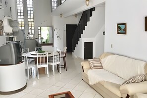 A modern living space with a dining area, a sofa, and a staircase.
