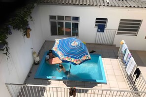 A swimming pool with a colorful umbrella, a white wall, and a window.