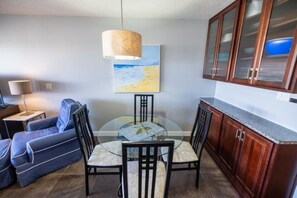 Ein Essbereich mit einem Glastisch, Stühlen, einem blauen Sofa, einer Lampe und Holzschränken.