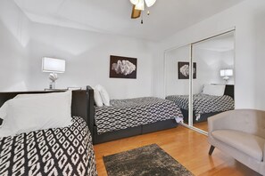 A modern bedroom with two beds, a bedside table, a chair, and artwork on the walls. - Coastal Condo Pool View + Heated Pool (St. Augustine)