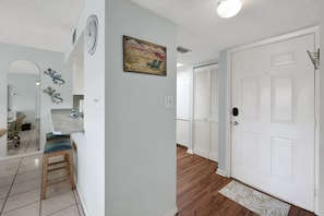 A hallway with a white door, a wooden floor, and a small rug. - Coastal Condo Pool View + Heated Pool (St. Augustine)