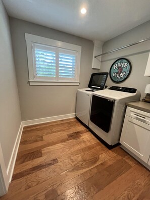 A compact kitchen with a washing machine, a dishwasher, a small refrigerator, and a window with blinds. - Spacious 3BR Home With Private Pool and Water Views in Yulee. Easy Access to Amelia Island (Yulee)