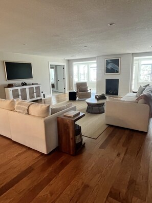 A spacious living room with a large sofa, a coffee table, and a television on a stand. There is a fireplace and a door leading to another room. - Spacious 3BR Home With Private Pool and Water Views in Yulee. Easy Access to Amelia Island (Yulee)
