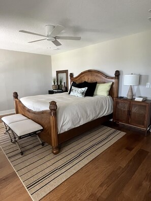A bedroom with a wooden bed, a nightstand, a lamp, a mirror, and a ceiling fan. - Spacious 3BR Home With Private Pool and Water Views in Yulee. Easy Access to Amelia Island (Yulee)