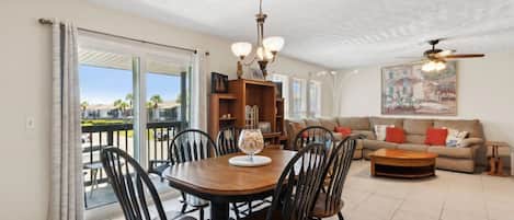 A dining area with a round table, chairs, and a chandelier. There is a sofa and a painting in the living area.
