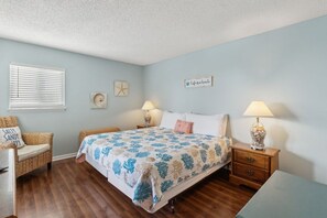 A bedroom with a bed, two bedside tables, a chair, and a small table. - Beachfront 2BR Pool Direct Access (Fernandina Beach)