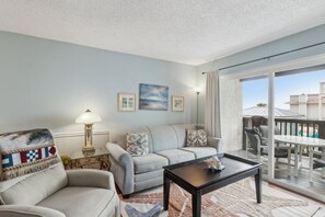 A living room with a sofa, a coffee table, and a view of the outside. - Beachfront 2BR Pool Direct Access (Fernandina Beach)