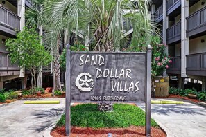 A sign for Sand Dollar Villas with a modern building in the background. - Beachfront 2BR Pool Direct Access (Fernandina Beach)