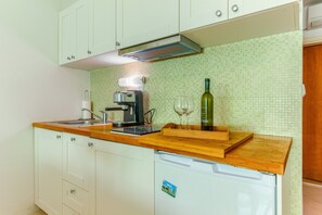 A kitchen with white cabinets, a wooden countertop, a coffee machine, two wine glasses, and a bottle of wine. - Two-bedroom apartment with garden, only 5 min walking to the Bacvice beach (Split)