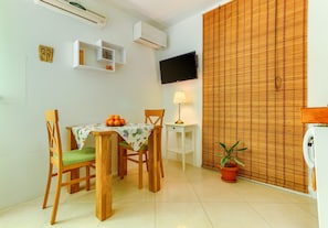 A dining area with a table, chairs, a television, a lamp, and a potted plant. - Studio apartment with garden, on 5 min walking to the Bacvice beach (Split)