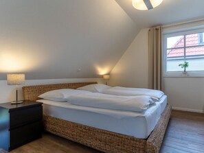 Ein Schlafzimmer mit Bett, Nachttischen, einer Lampe, einem Fenster mit Blick auf Gebäude und einer kleinen Pflanze im Fensterbrett.