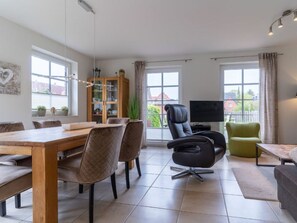 A modern living room with a dining area, a television, and a view of the outside. - Holiday Home With 2 Bedrooms (St. Peter-Ording)