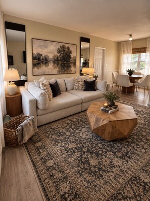 A living room with a sofa, coffee table, and a large painting on the wall. - CASA CAMEO European-Inspired Tampa Stay (Tampa)