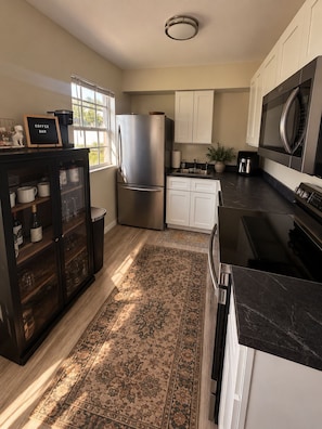 A modern kitchen with a refrigerator, microwave, and stove, wooden cabinets, a coffee bar, and a rug. - CASA CAMEO European-Inspired Tampa Stay (Tampa)