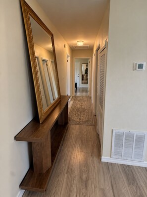 A hallway with a wooden bench, a large mirror, and a patterned rug leading to a door. - CASA CAMEO European-Inspired Tampa Stay (Tampa)