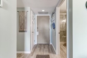 A hallway with a wooden floor, a door at the end, and a wall with a macrame curtain. - Ocean View 2BR Pool Walk to Beach (Fernandina Beach)