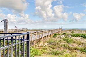 A wooden boardwalk extending into the distance with a metal railing on one side, surrounded by grassy terrain and a clear sky. - Ocean View 2BR Pool Walk to Beach (Fernandina Beach)
