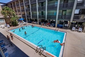 A swimming pool surrounded by lounge chairs and umbrellas, with a multi-story building in the background. - Ocean View 2BR Pool Walk to Beach (Fernandina Beach)