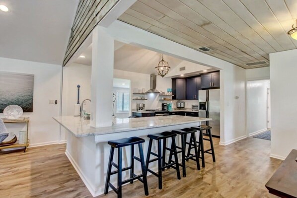 A modern kitchen with a central island, bar stools, and a view into the dining area. - 4BR Retreat Fire Pit 1 Mile to Beach (Fernandina Beach)