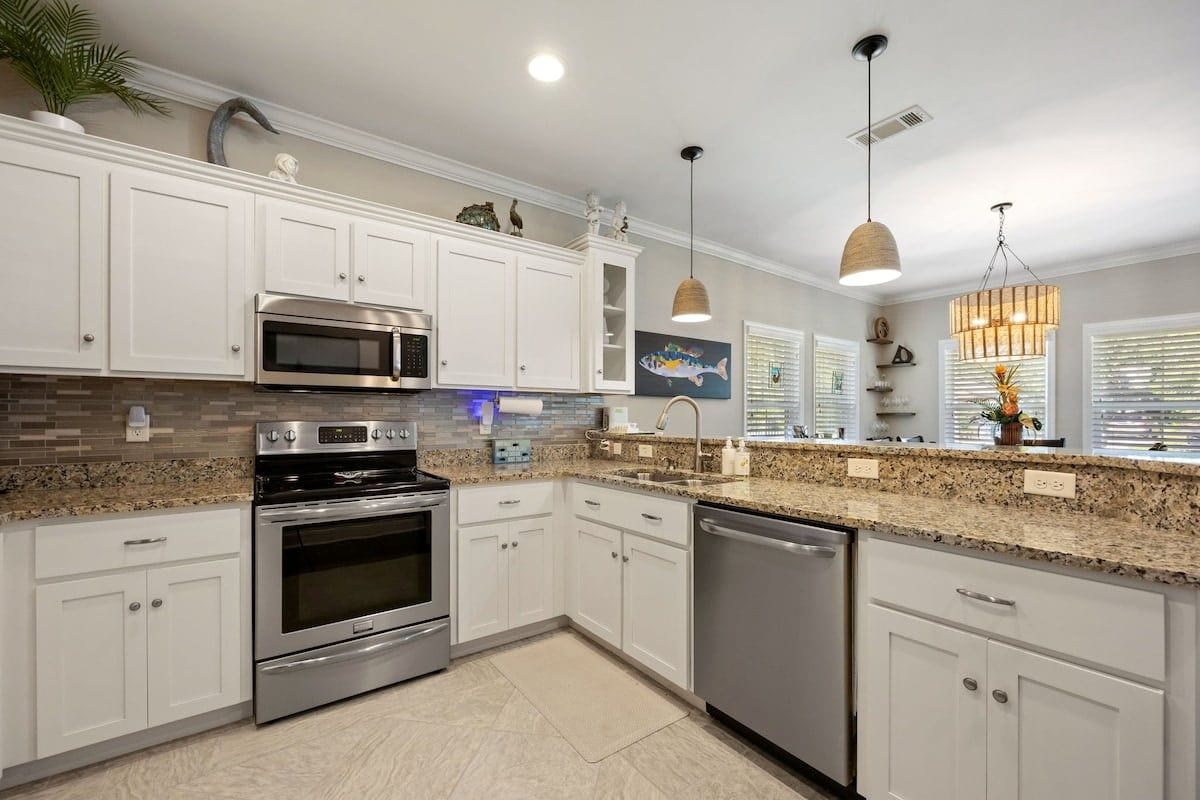 A modern kitchen with white cabinets, stainless steel appliances, granite countertops, and pendant lighting.