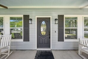 A front door with a dark-colored door and two windows with shutters, a welcome mat, and two rocking chairs. - The Helm on Elm Beautiful 3/2 Near Downtown (Fernandina Beach)