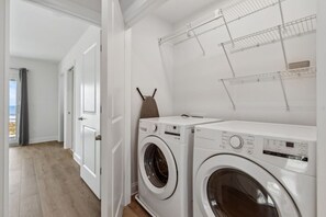A laundry area with two front-loading washing machines, a drying rack, and a door leading to a room with a view. - Brand New 4BR Ocean Views Pool (Fernandina Beach)