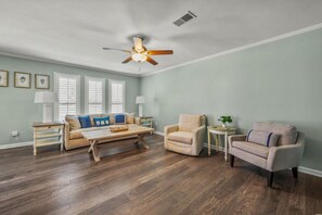 Ein geräumiges Wohnzimmer mit Deckenventilator, einer Sofagarnitur, einem Couchtisch und einem Beistelltisch mit Lampe.