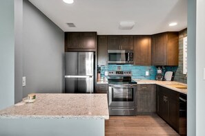 A modern kitchen with stainless steel appliances, dark wooden cabinets, and a blue backsplash. - 6507 Fernandina Shores (Fernandina Beach)