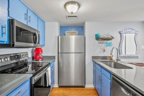 A modern kitchen with blue cabinets, stainless steel appliances, and a wooden floor. - Oceanfront 2BR Pool Walk Beach Sleeps 6 (Fernandina Beach)