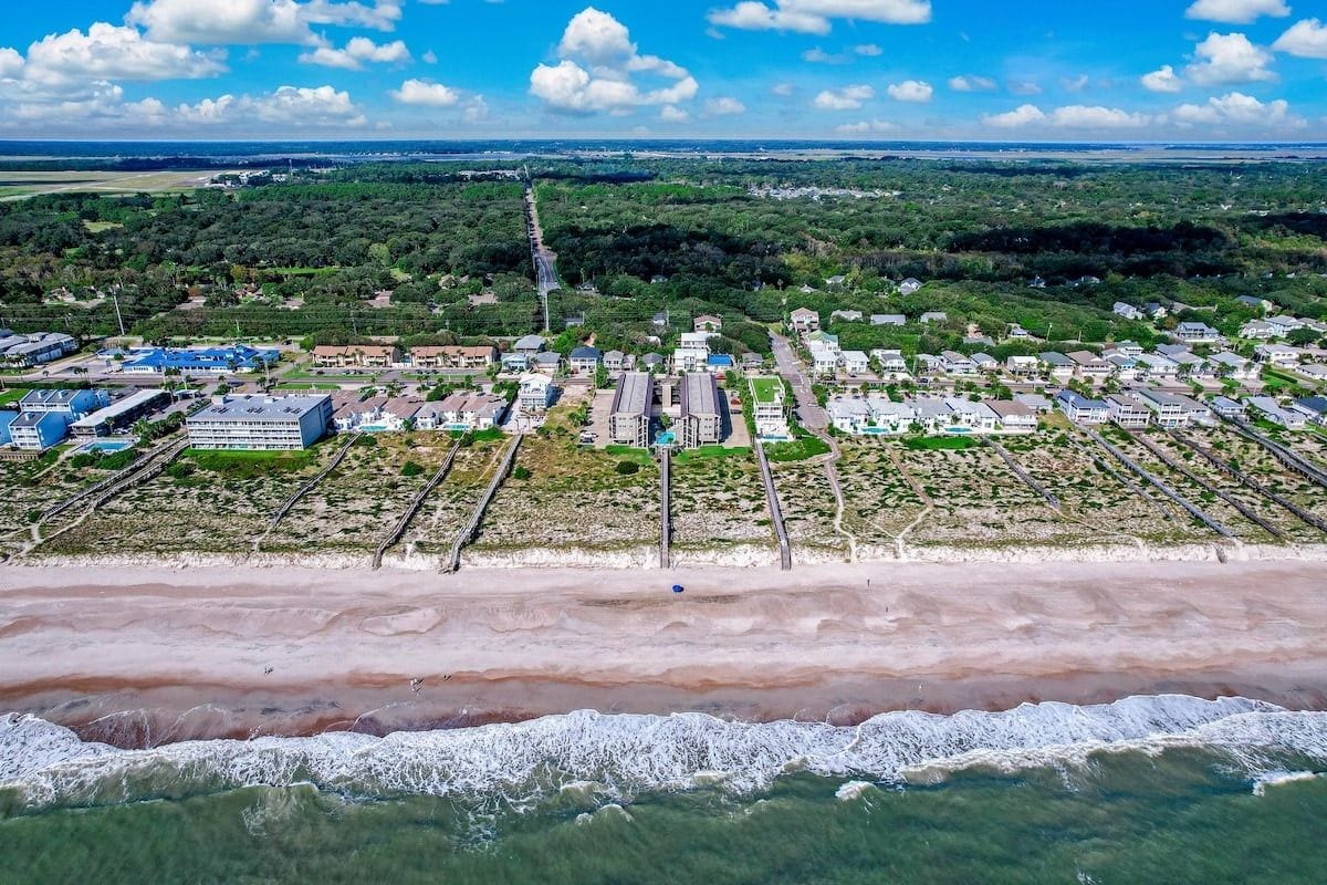 An aerial view of a coastal town with residential areas, a beach, and a clear sky.