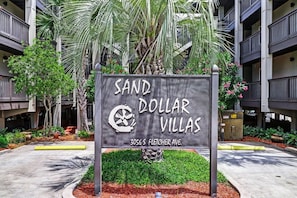 A sign for Sand Dollar Villas with a modern building in the background. - Beachfront Condo Pool Sleeps 6 (Fernandina Beach)