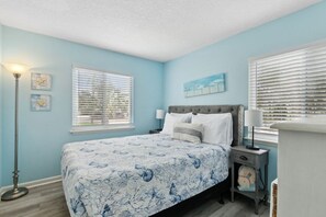 A bedroom with a bed, two bedside tables, a floor lamp, and a window with blinds. - Beachfront Condo Pool Sleeps 6 (Fernandina Beach)