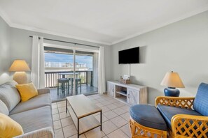 Ein Wohnzimmer mit einer Couch, einem Tisch, einem an der Wand befestigten Fernseher und einem Balkon mit Blick.