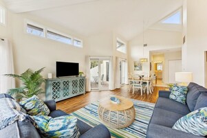 Uma sala de estar espaçosa com sofá, televisão e área de jantar com cadeiras e mesa.
