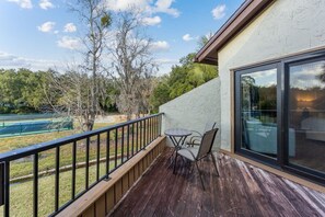 Varanda com mesa e cadeiras, com vista para uma quadra de tênis e árvores.