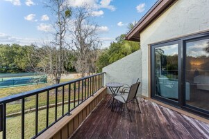 Varanda com mesa e cadeiras, com vista para uma quadra de tênis e árvores.