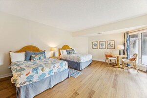 Quarto de hotel com duas camas, uma mesa de jantar e cadeiras, e uma janela grande.