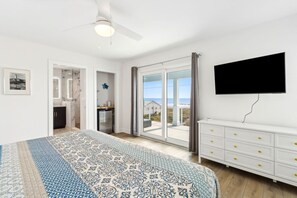 Ein Schlafzimmer mit einem Bett, einem Fernseher, einer Schiebetür zum Balkon und einer weißen Kommode.