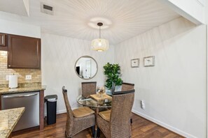 A dining area with a glass table, wicker chairs, a hanging light fixture, and a potted plant. - Dog-friendly 3BR Walk to Beach Pool (Fernandina Beach)