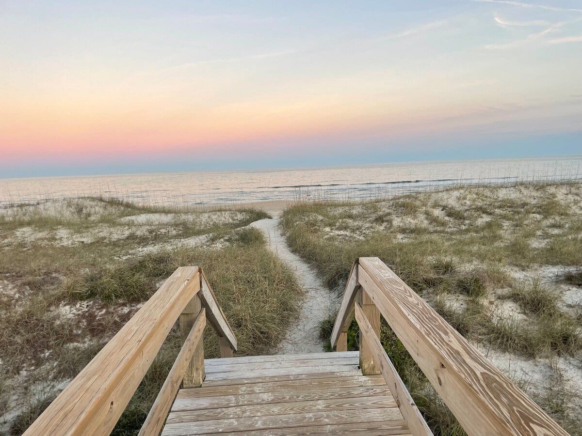 A wooden boardwalk leading to a beach with sand dunes.