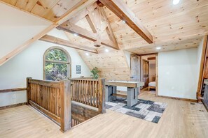 Ein Schlafzimmer im Spitzboden mit schrägem Dach, einem Holztisch, einer Sitzbank und Blick auf Bäume durch ein großes Fenster.