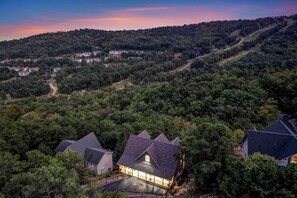 A residential area with houses surrounded by dense forest, a winding road, and a hill in the background. - New Build w/ Views, Hot Tub, & Sauna. Sleeps 16 (Massanutten)