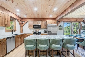A kitchen with wooden cabinets, stainless steel appliances, and a bar area with stools. - New Build w/ Views, Hot Tub, & Sauna. Sleeps 16 (Massanutten)