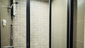 Eine begehbare Dusche mit Glastür, gefliesten Wänden und einer Duschbrause.