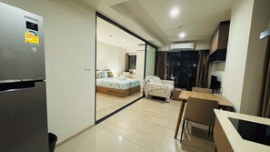 Ett modernt hotellrum med ett Samsung-kylskåp, en säng med ett blått, blommigt sängöverkast, en separat sittgrupp med bord och stolar samt ett stort fönster.