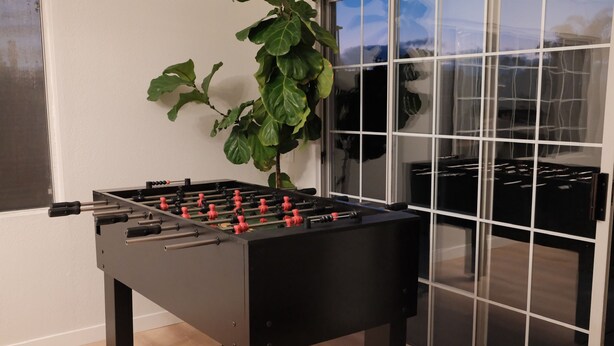 Una taula de futbolí a una habitació amb un finestral gran i una planta.