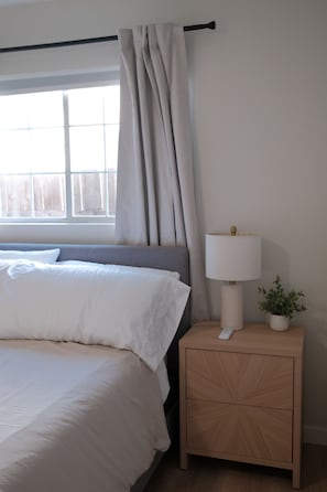A bedroom with a bed, a nightstand with a lamp, and a window with curtains. - Modern SD Home / Sleeps 6 / Fast WiFi / Beach within 10 miles / Games + BBQ (San Diego)